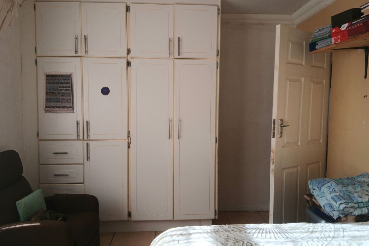 A bedroom featuring built-in white cupboards, tiled flooring, and a standard panel door, offering functional storage space.