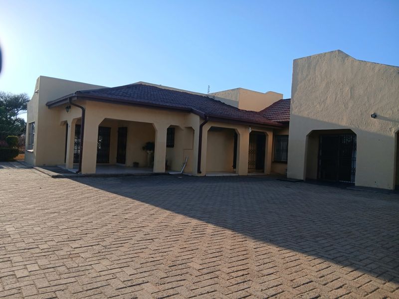 Front exterior view of the house featuring a large paved driveway, covered patio area, and tiled roof structure.