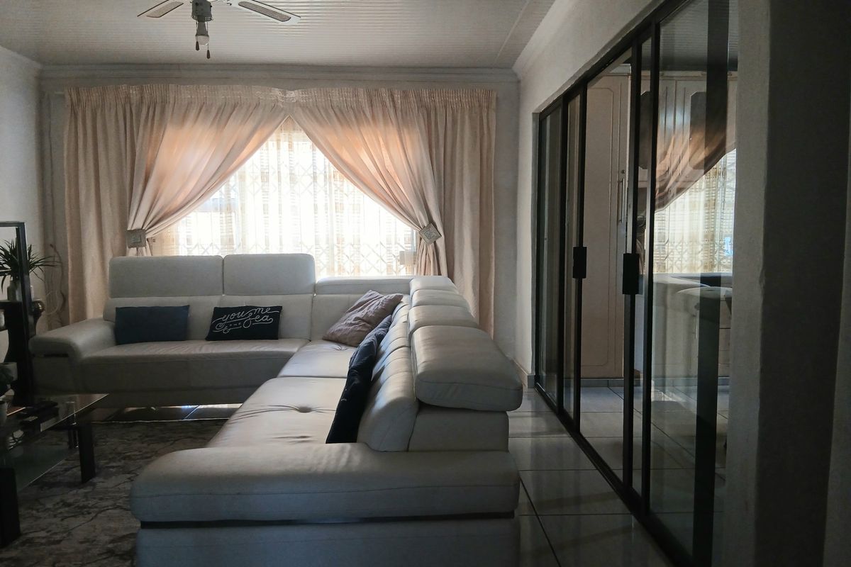 A living room featuring tiled flooring, a ceiling fan, and large sliding glass doors that provide access to an adjacent space.