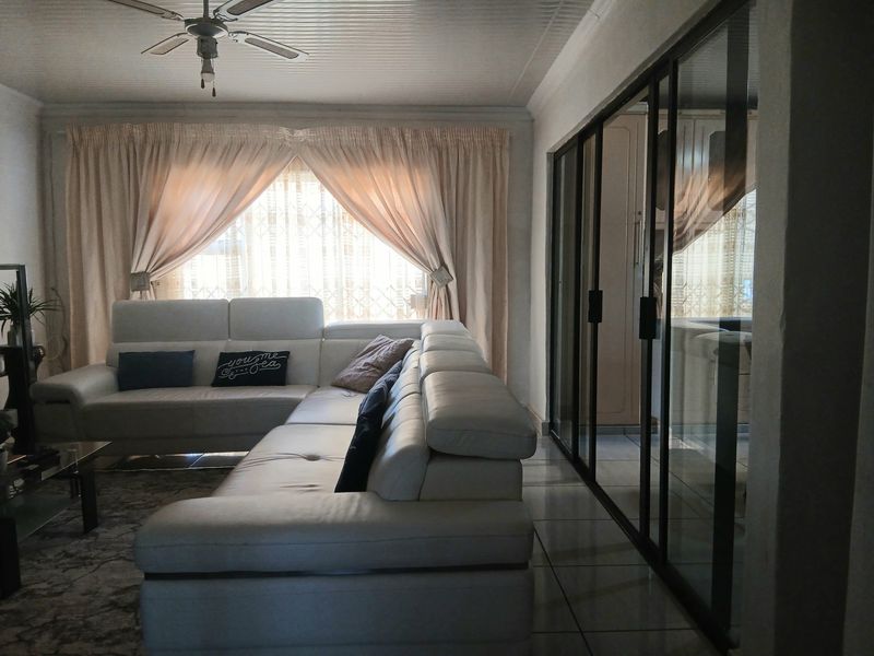A living room featuring tiled flooring, a ceiling fan, and large sliding glass doors that provide access to an adjacent space.