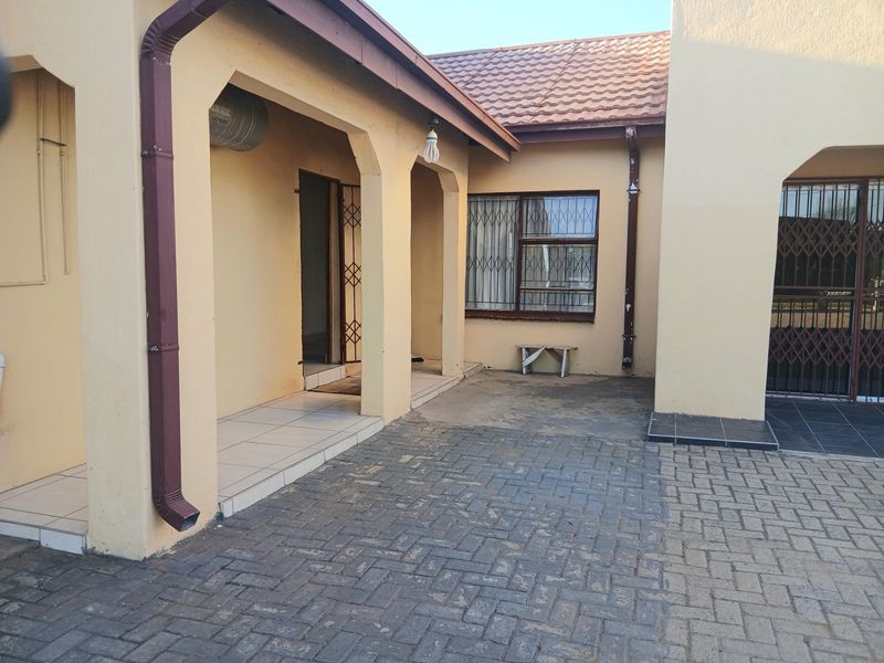 A paved rear courtyard area featuring a covered patio, security gates, and tiled roof finishes, providing a functional outdoor space.