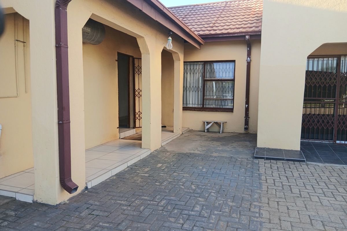 A paved rear courtyard area featuring a covered patio, security gates, and tiled roof finishes, providing a functional outdoor space.
