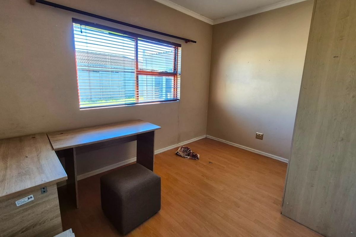 A functional bedroom featuring laminate flooring, a built-in wardrobe, and a window with venetian blinds, offering a neutral canvas for personalization.