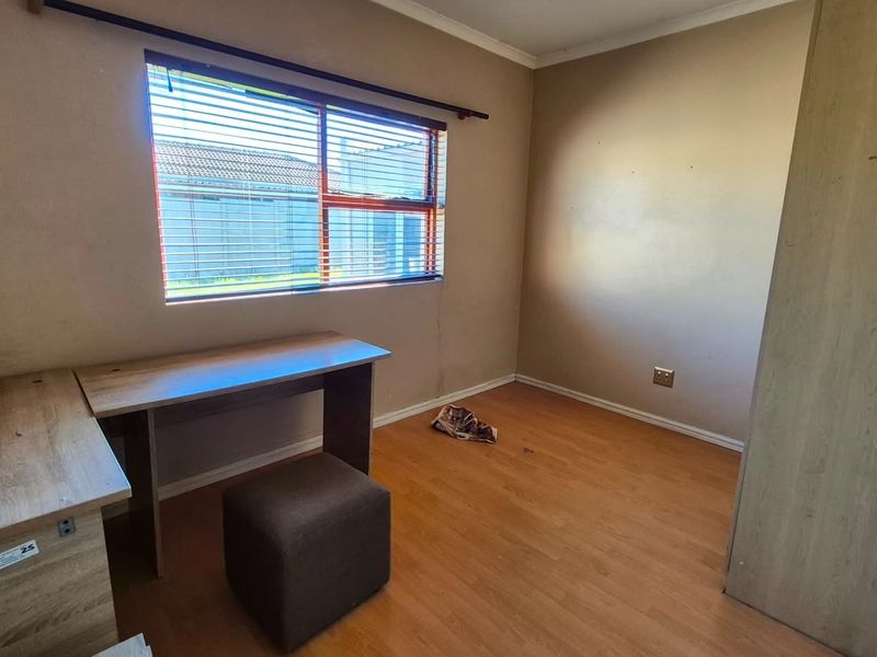 A functional bedroom featuring laminate flooring, a built-in wardrobe, and a window with venetian blinds, offering a neutral canvas for personalization.
