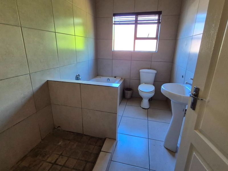 A functional bathroom featuring a pedestal basin, toilet, built-in bathtub, and a walk-in shower area with tiled finishes throughout.