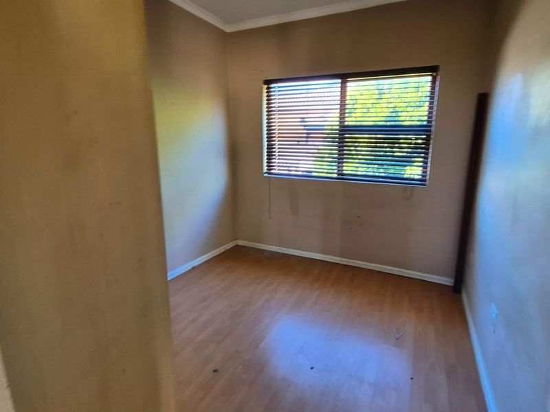 An empty bedroom featuring laminate flooring and venetian blinds, requiring minor cosmetic updates to the wall finishes.