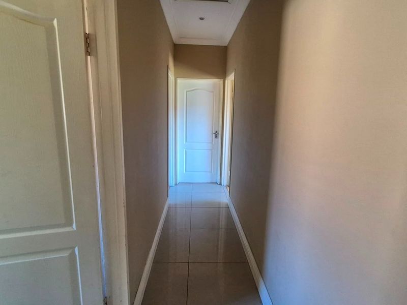 A clean and well-maintained hallway featuring neutral wall tones, tiled flooring, and multiple internal doors leading to adjacent rooms.