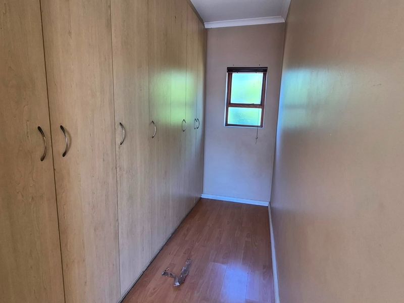 A narrow bedroom featuring extensive built-in wooden cupboards and laminate flooring, providing ample storage space.