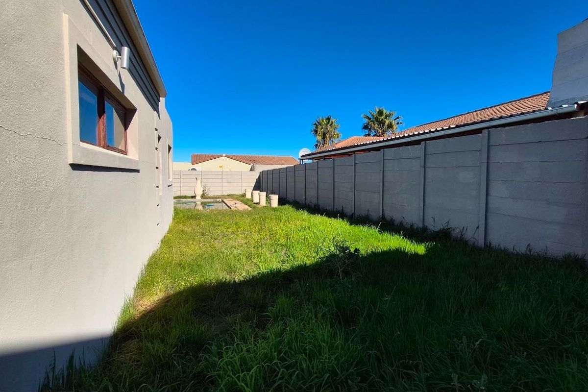 Rear garden area featuring a swimming pool, precast concrete boundary walls, and a plastered exterior wall with timber window frames.