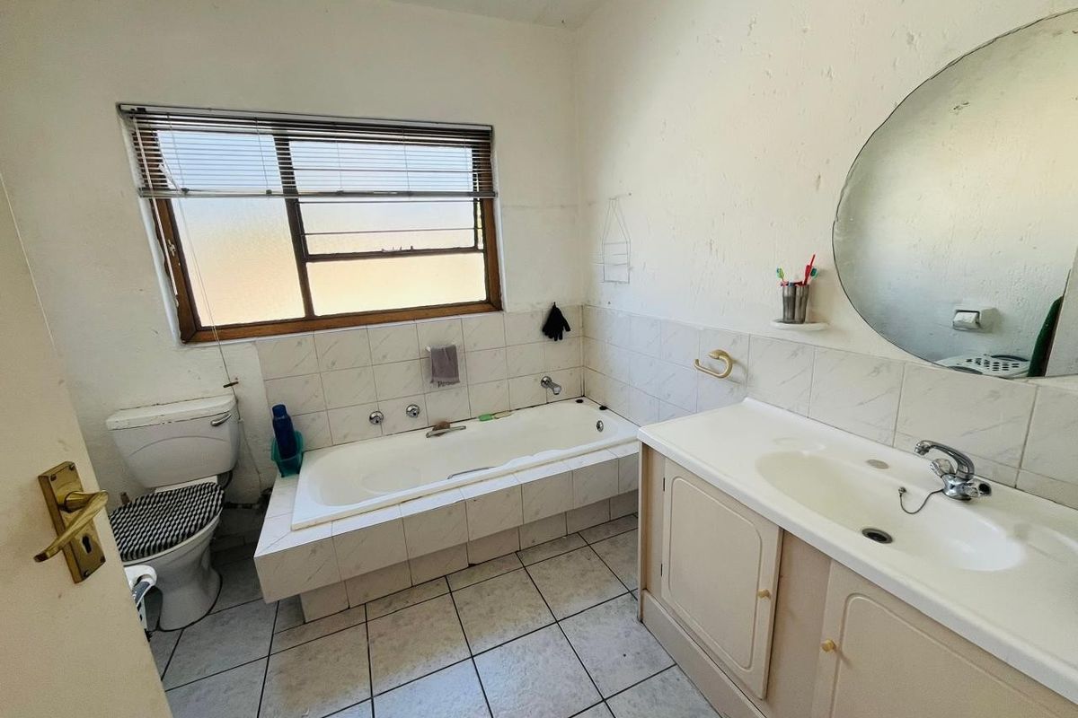 A dated bathroom featuring a built-in bathtub, vanity cabinet with basin, and toilet, requiring cosmetic updates to modernize the space.