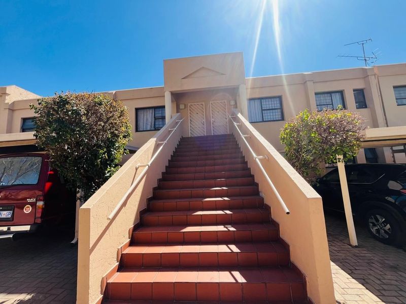 Front elevation of a multi-unit residential building featuring a central tiled staircase with metal handrails leading to upper-level entrance doors.