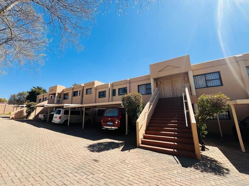 Front elevation of a multi-unit residential building featuring a paved driveway, covered carports, and an external staircase leading to upper-level entrances.
