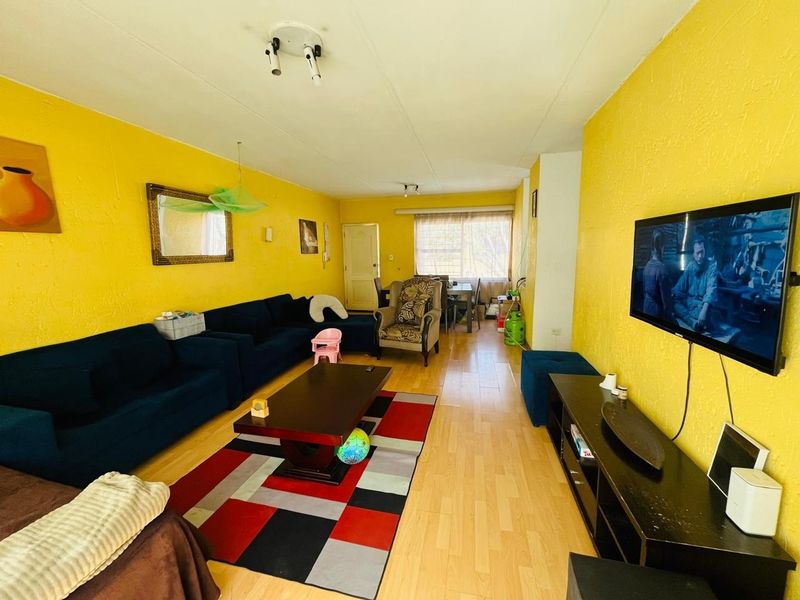 A spacious living room featuring laminate flooring and bright yellow textured walls, offering a functional layout for family living.