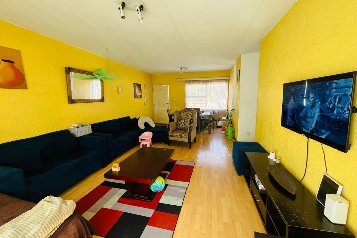 A spacious living room featuring laminate flooring and bright yellow textured walls, offering a functional layout for family living.