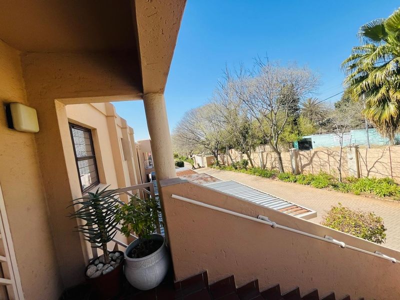 An elevated outdoor balcony area featuring a tiled staircase with a metal handrail, overlooking the driveway and surrounding garden area.
