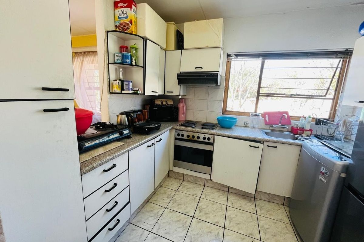 A functional kitchen featuring white cabinetry, laminate countertops, a built-in oven with hob, and tiled flooring, offering potential for a modern renovation.
