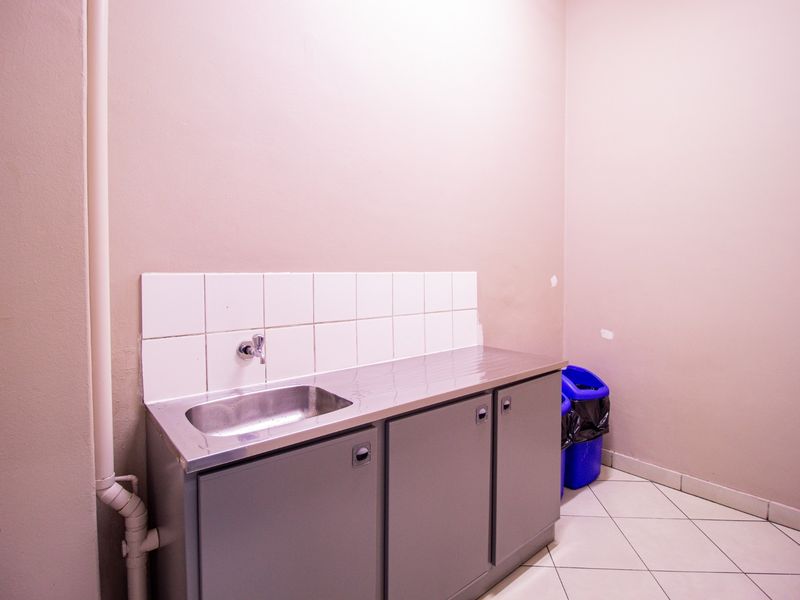 A functional utility or scullery area featuring a stainless steel sink, built-in cabinetry, tiled splashback, and tiled flooring.