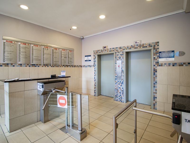 Commercial building lobby featuring a reception desk, security turnstiles, and dual elevator access with a directory board for office tenants.