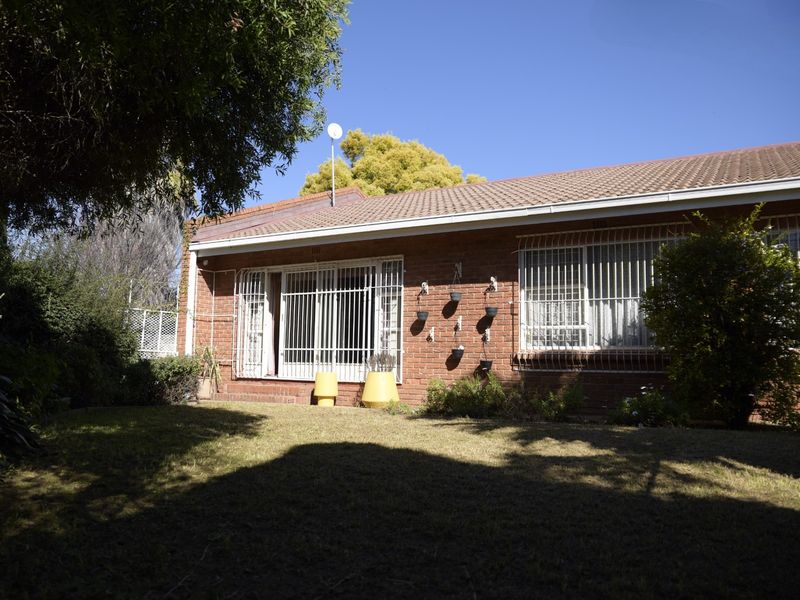 Rear view of a brick townhouse featuring a tiled roof, security bars on windows and doors, and a private garden area.