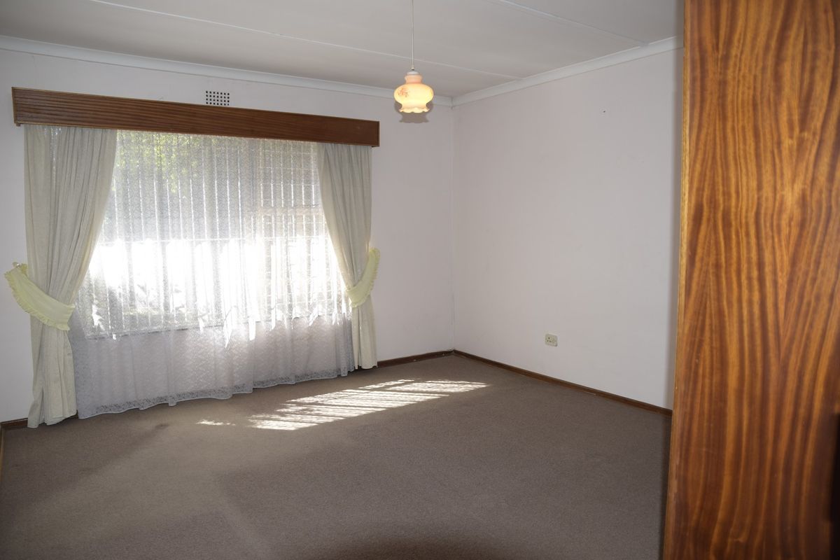 A spacious, empty bedroom featuring neutral carpet flooring, a coved ceiling, and a large window with a wooden pelmet.