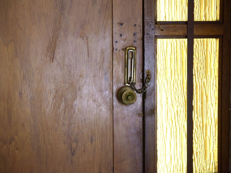 Close-up view of a vintage timber entrance door featuring a textured glass sidelight and traditional security hardware.
