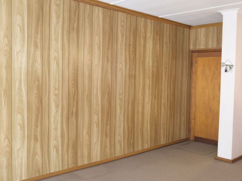 An empty living area featuring dated wood paneling on the walls and a timber door, offering a blank canvas for modern renovation.
