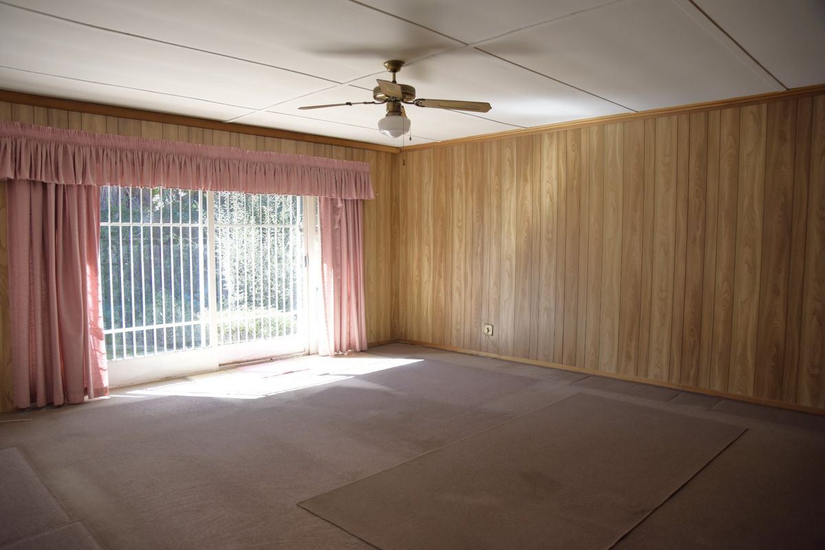 Spacious living room featuring wood paneling, a ceiling fan, and sliding glass doors with security gates leading to the exterior.