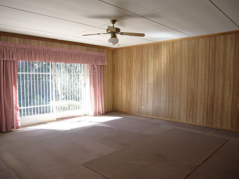 Spacious living room featuring wood paneling, a ceiling fan, and sliding glass doors with security gates leading to the exterior.