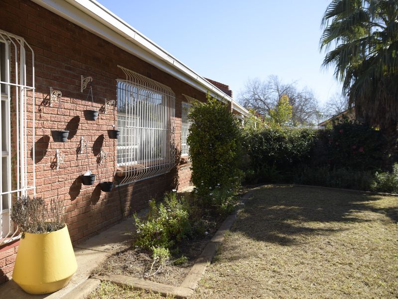 A view of the rear exterior of the townhouse featuring a face brick facade, security bars on windows, and a landscaped garden area.