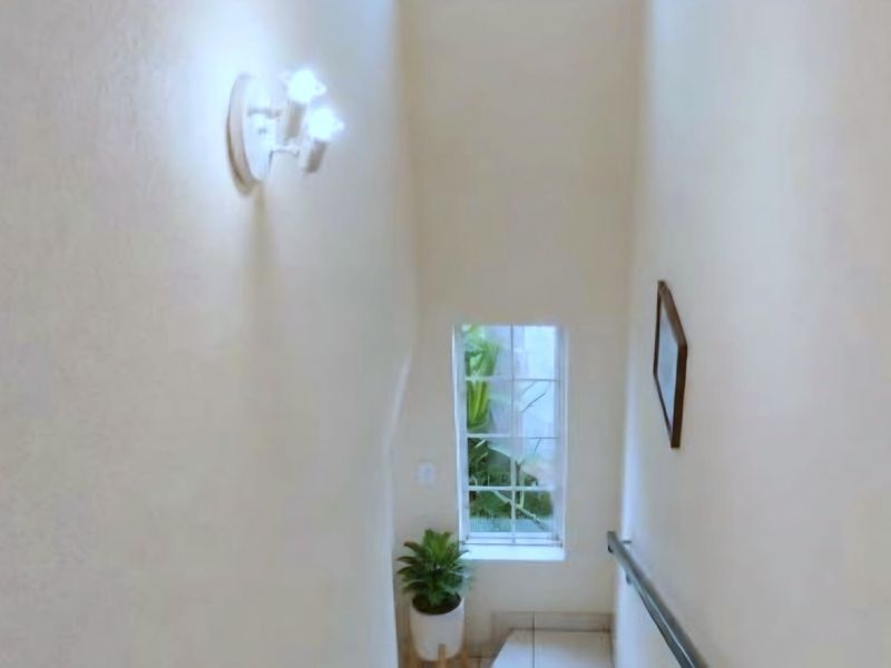 A bright staircase hallway featuring a window with garden views, a wall-mounted light fixture, and a sturdy handrail.