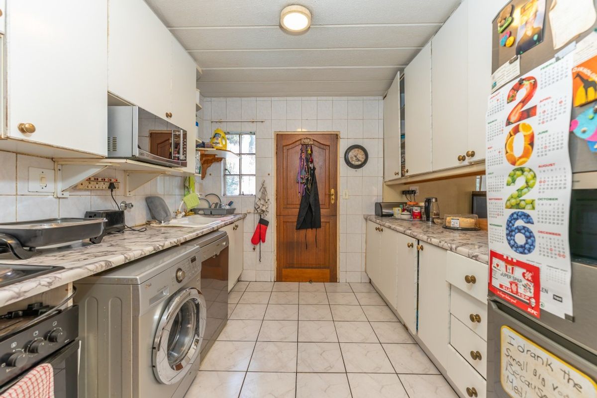 A functional galley-style kitchen featuring laminate countertops, tiled backsplash, and ample built-in cabinetry, providing a practical workspace for daily meal preparation.