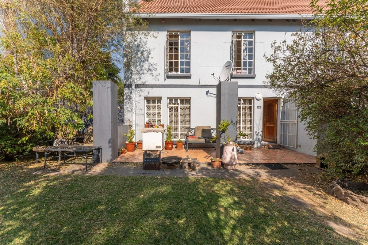 Rear view of the townhouse featuring a tiled patio area, garden space, and traditional casement windows with a secure entrance.