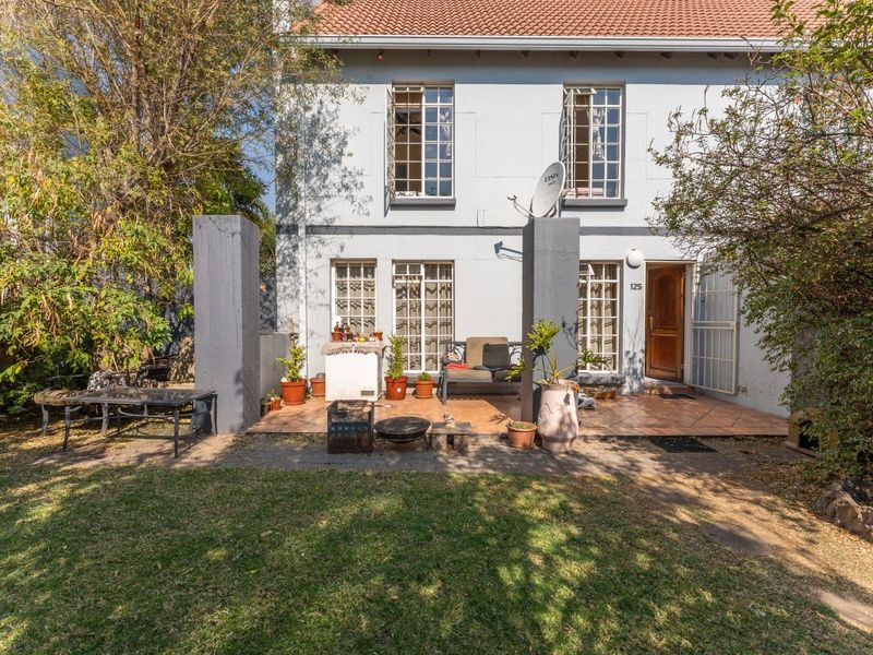 Rear view of the townhouse featuring a tiled patio area, garden space, and traditional casement windows with a secure entrance.
