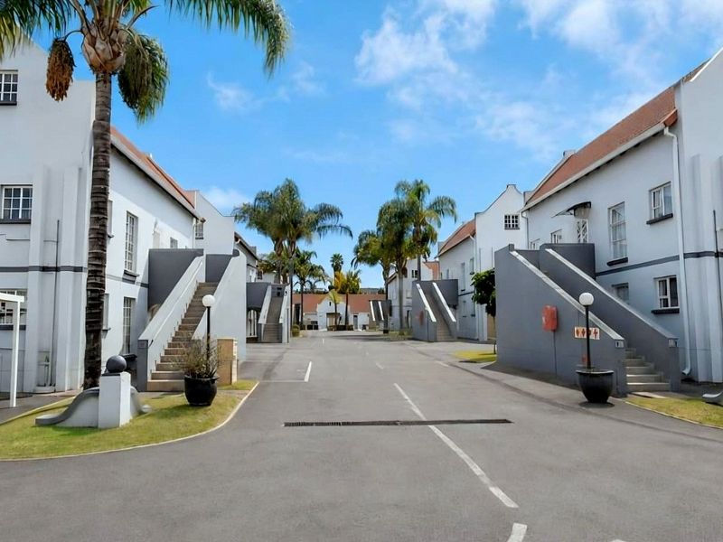 A view of the townhouse complex driveway featuring white facades, external staircases, and paved access roads with established palm trees.