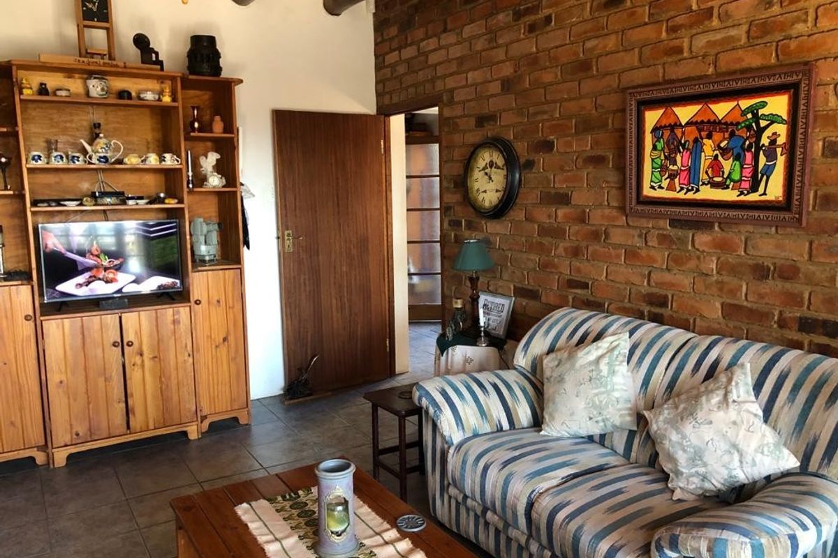 A cozy living room featuring rustic exposed brick walls, timber ceiling beams, and tiled flooring, creating a warm and traditional atmosphere.