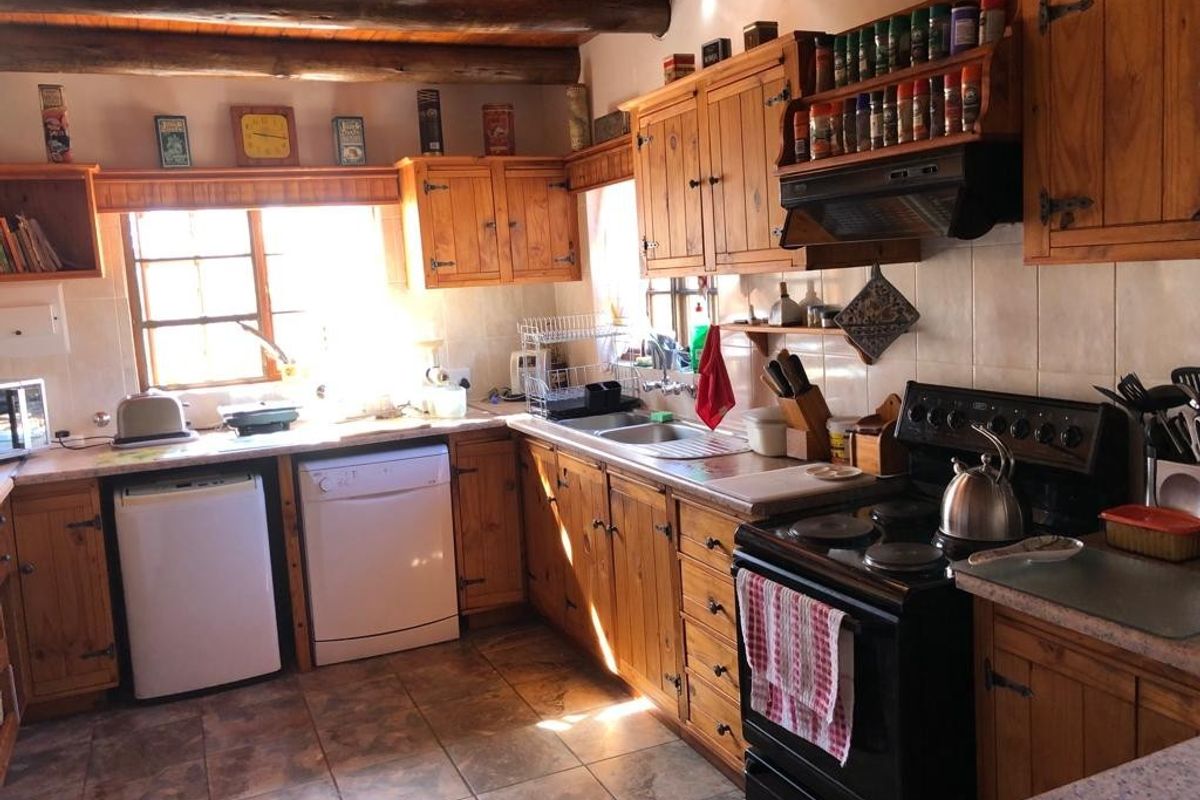 A rustic kitchen featuring wooden cabinetry, exposed timber ceiling beams, tiled flooring, and a functional layout with integrated stove and extractor fan.