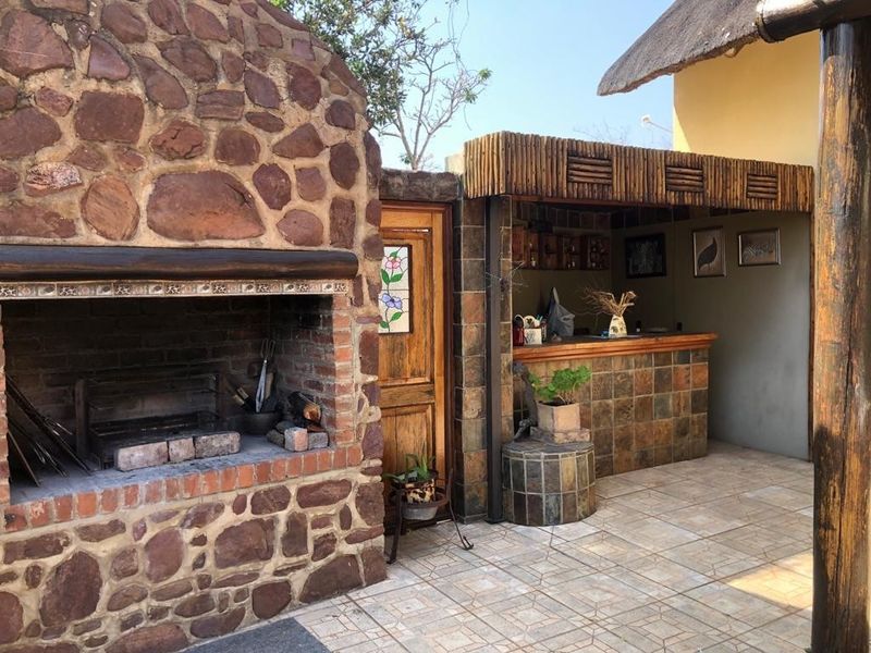 Outdoor entertainment area featuring a rustic stone built-in braai, a tiled bar counter, and a thatched roof covering.