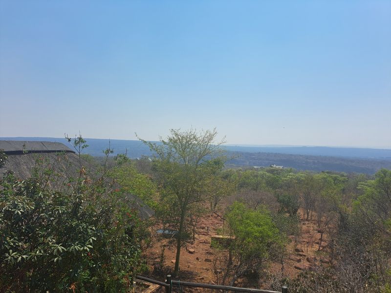 A scenic elevated view overlooking a natural bushveld landscape with a partial view of a thatched roof structure.