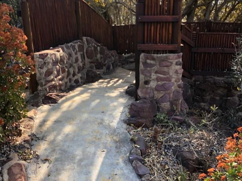 A garden pathway featuring stone retaining walls and timber pole fencing, leading through a landscaped outdoor area.