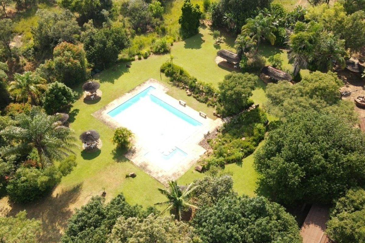 Aerial view of a spacious property featuring a large swimming pool, paved surround, and extensive landscaped gardens with multiple thatched outdoor seating areas.