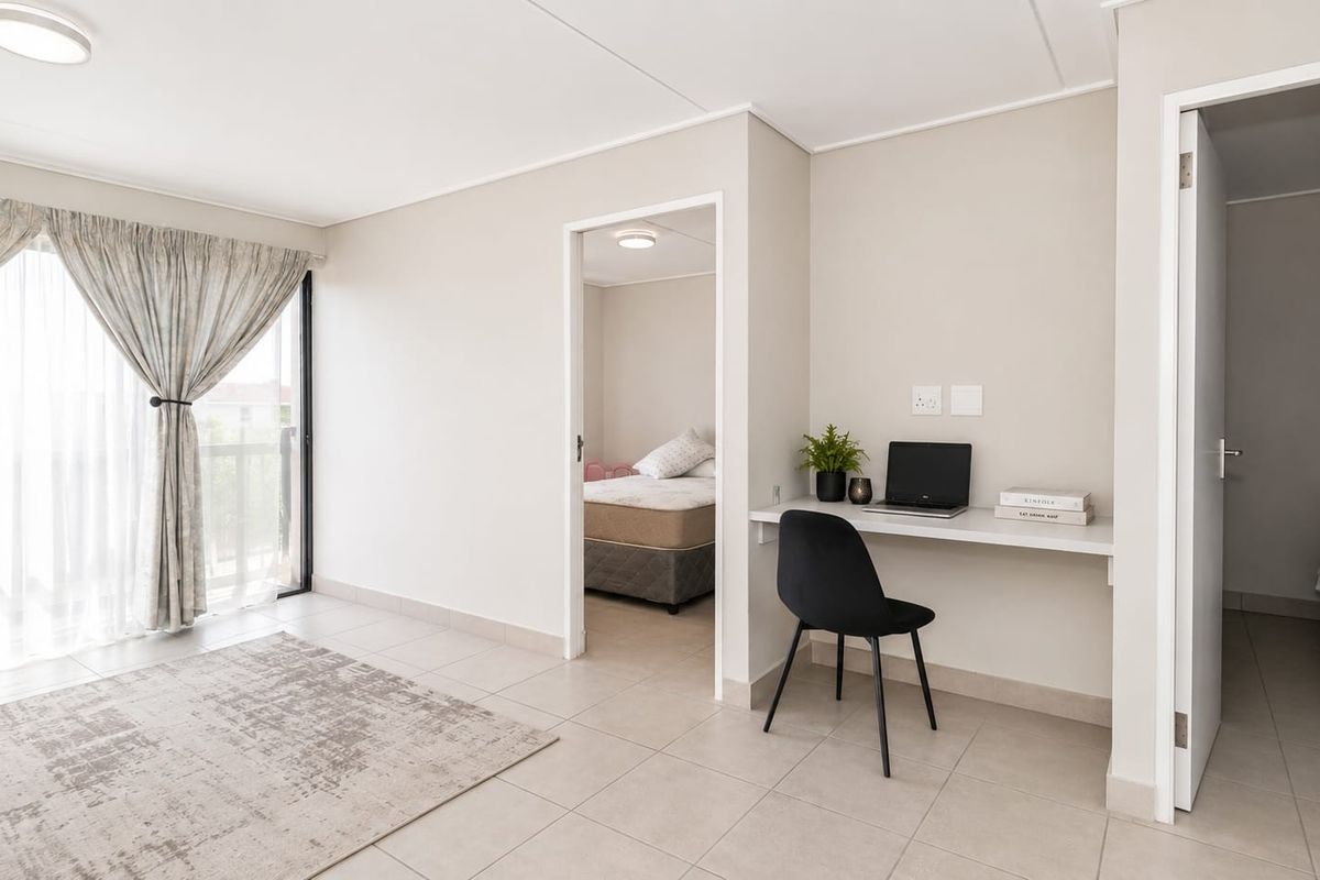 A bright living area featuring neutral tiled flooring, a built-in desk workspace, and a sliding glass door leading to an outdoor space.