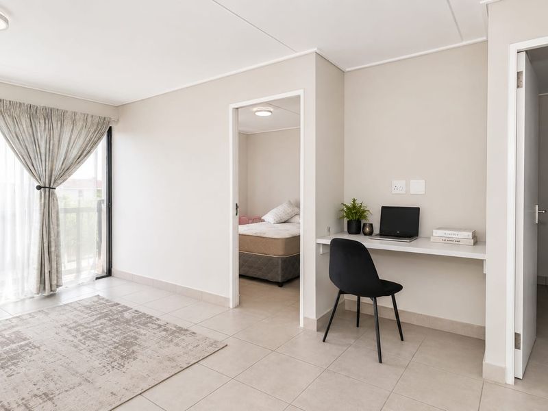 A bright living area featuring neutral tiled flooring, a built-in desk workspace, and a sliding glass door leading to an outdoor space.