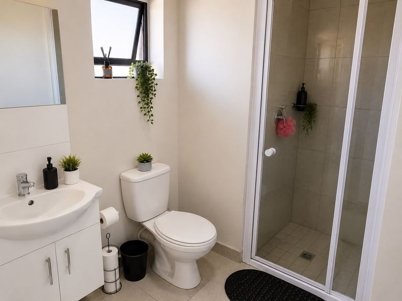 A clean and modern bathroom featuring a vanity cabinet, toilet, and a glass-enclosed shower with neutral wall tiling.