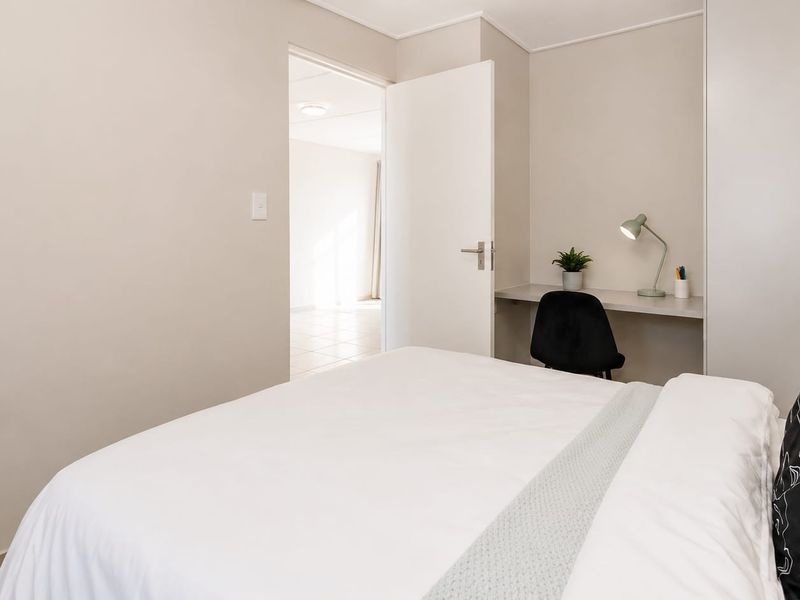 A well-maintained bedroom featuring a built-in wardrobe and a convenient integrated desk area, with neutral finishes and clean lines.