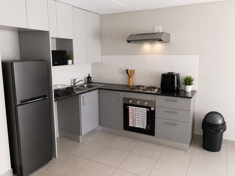Modern kitchen featuring grey and white cabinetry, dark countertops, built-in oven, electric hob, extractor fan, and tiled flooring.