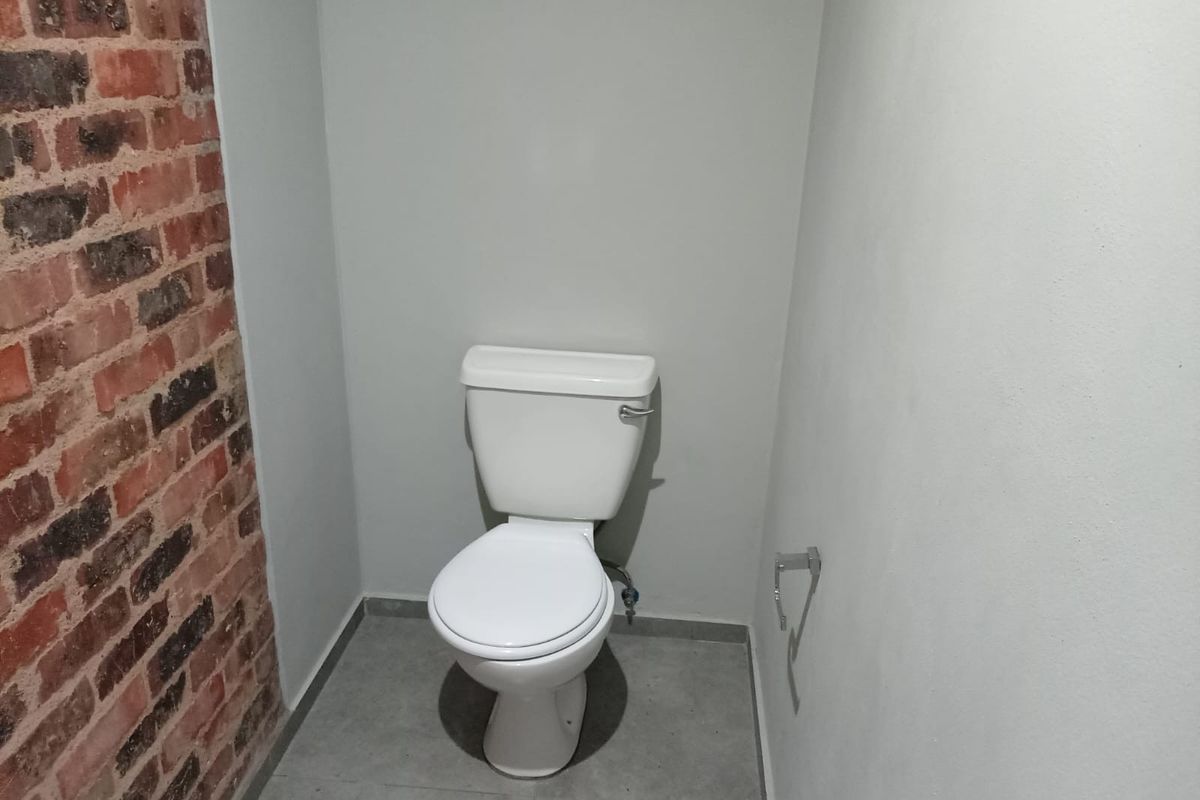 A compact bathroom featuring a modern toilet, grey tiled flooring, and a characterful exposed brick feature wall.