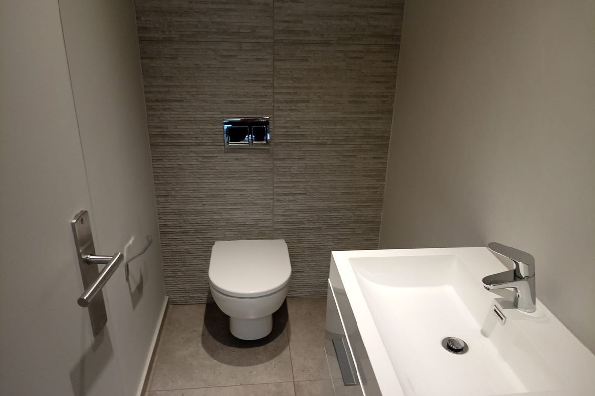 Modern guest bathroom featuring a wall-hung toilet with concealed cistern, tiled feature wall, and a sleek vanity basin with mixer tap.
