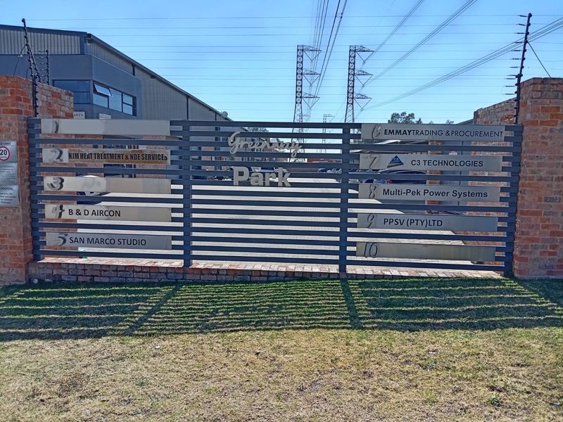 Front entrance view of Greenway Park business complex featuring a brick perimeter wall, electric fencing, and a directory sign for multiple commercial tenants.
