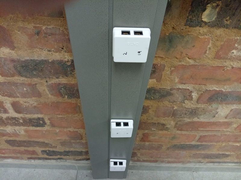 A close-up view of data trunking mounted on an exposed brick wall, featuring multiple CAT6 ethernet connection ports for office connectivity.