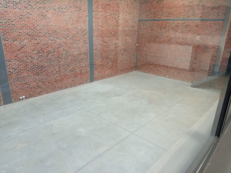 A spacious, empty open-plan area featuring industrial-style exposed brick walls, polished concrete flooring, and a modern glass balustrade.